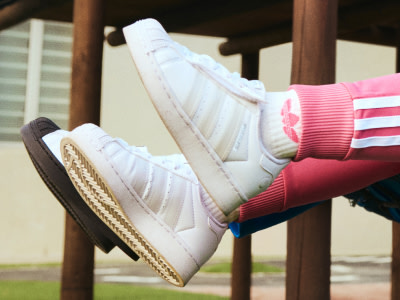 A pair of white sneakers with pink and white striped socks resting on a wooden bench against a blurred outdoor background.