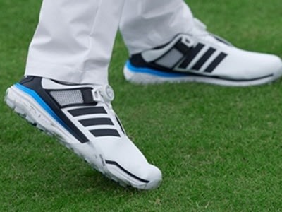 The image shows a pair of white and blue athletic shoes on a grassy field.