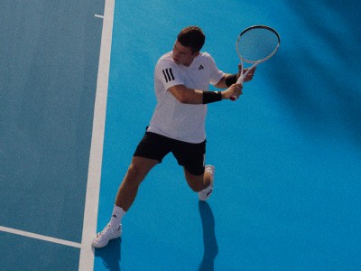 Une personne en chemise blanche et short noir joue au tennis sur un court bleu.
