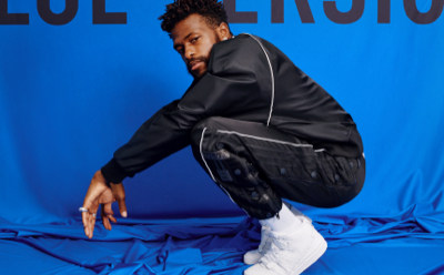 Una persona con chaqueta y pantalones negros está agachada sobre un fondo azul.