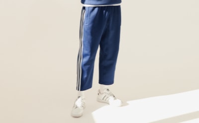 Un pantalón deportivo en azul marino con rayas blancas en los laterales, combinado con zapatillas blancas, sobre un fondo liso beige.
