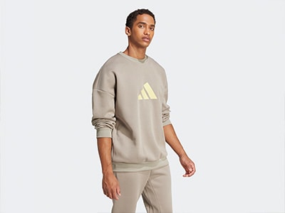 A young man wearing a beige sweatshirt with the Adidas logo stands against a plain white background.