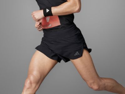 The image shows a person wearing black athletic shorts and a black shirt, with a red wristband on their arm, standing against a plain gray background.