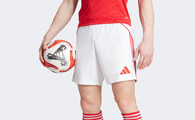 The image shows a person wearing a red jersey and white shorts, holding a soccer ball. The background appears to be a plain, light-colored surface.