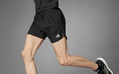The image shows a person's lower body wearing black athletic shorts and shoes against a plain gray background.