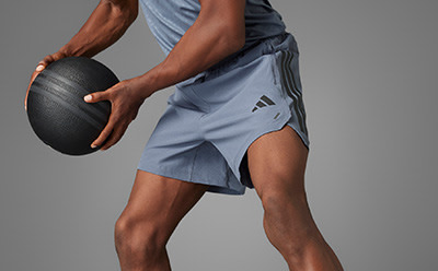 A person in athletic clothing holds a black medicine ball, standing against a plain gray background.