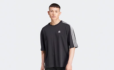 A young man wearing a black t-shirt with white stripes on the sleeves stands against a plain white background.