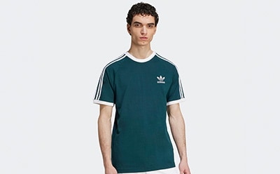 A young man wearing a green Adidas t-shirt stands against a plain white background.