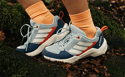 A pair of gray and orange athletic shoes with white soles are visible in the foreground, set against a background of lush greenery.