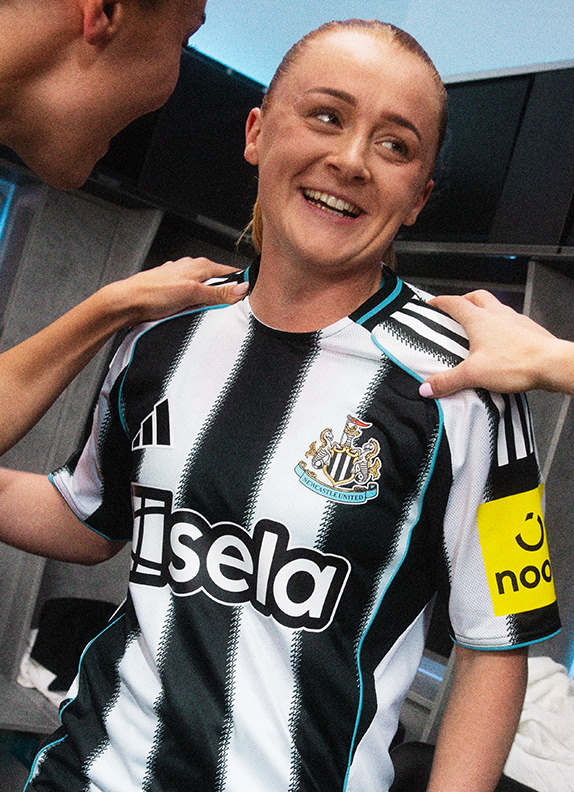 The image shows a person, likely a woman, wearing a black and white striped jersey with the text "Aisela" on it, smiling and posing for the camera in what appears to be a locker room or similar setting.