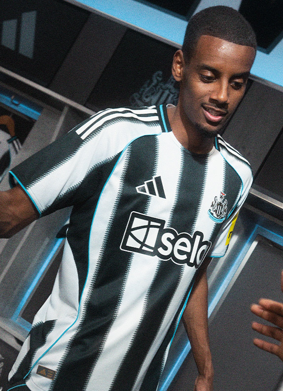 A smiling young man wearing a black and white soccer jersey with the team's logo prominently displayed, standing in front of a dark background with blue and white accents.