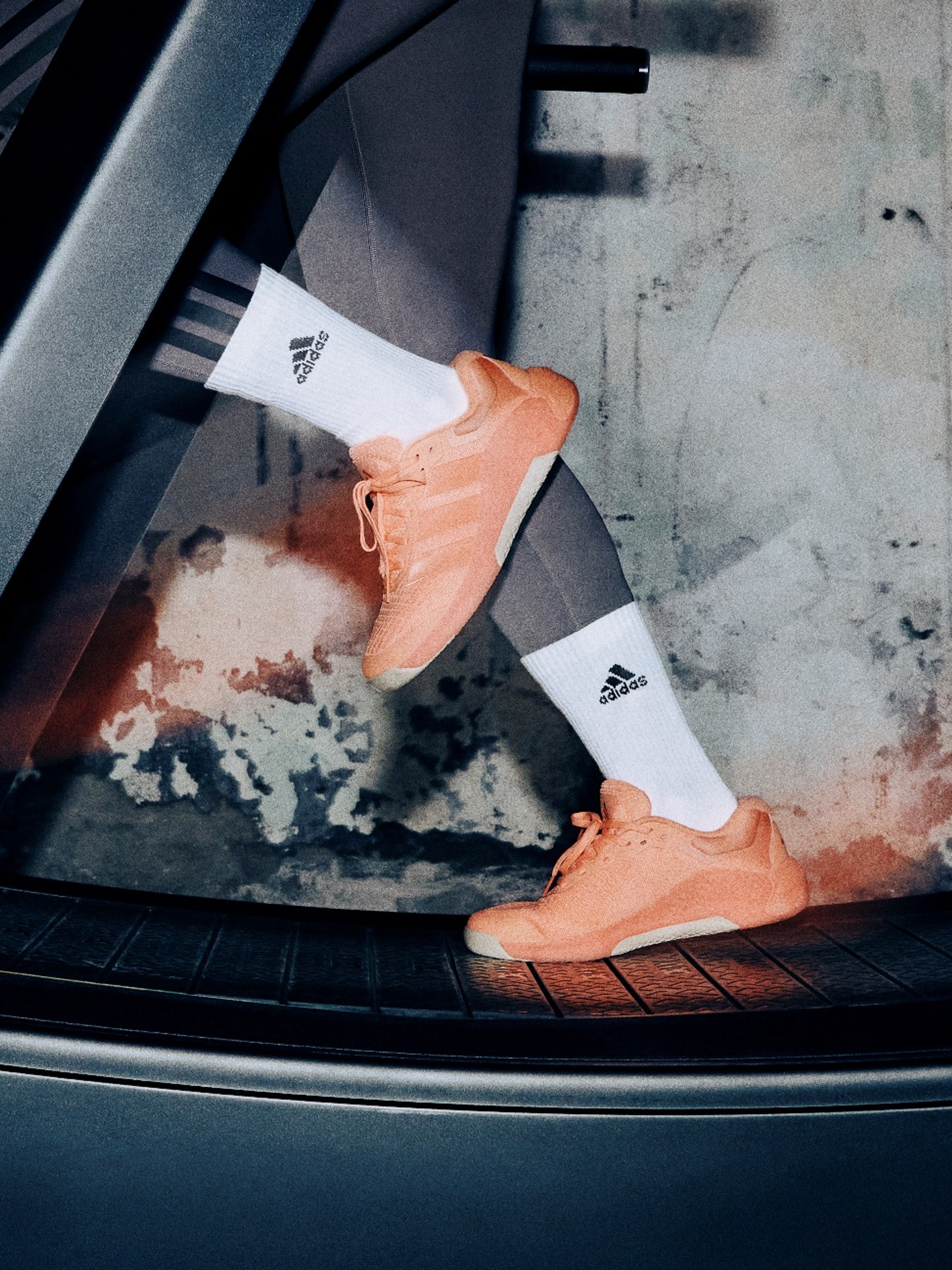 The image shows a pair of orange sneakers with white socks against a blurred, textured background.