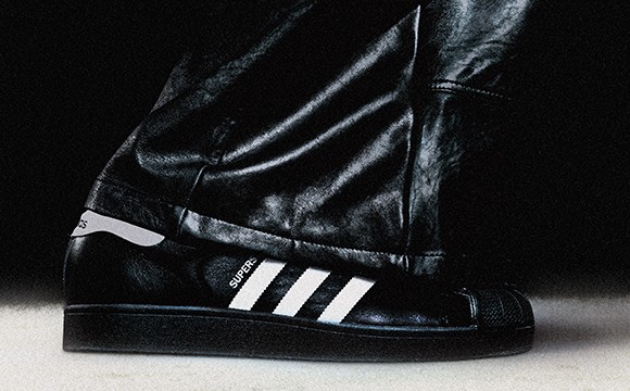 A close-up view of a person's foot wearing a black leather boot with the iconic three-stripe design of the Adidas brand prominently displayed.