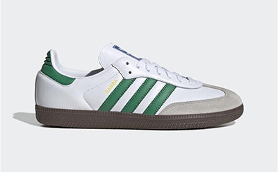 A pair of white and green Adidas sneakers with a gum sole is displayed against a plain white background.