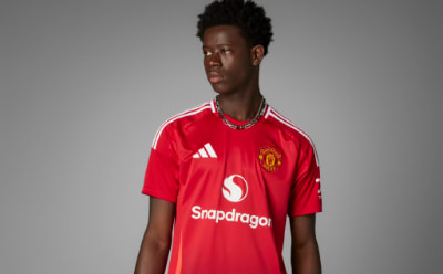 A young man wearing a red Manchester United soccer jersey stands against a plain gray background.