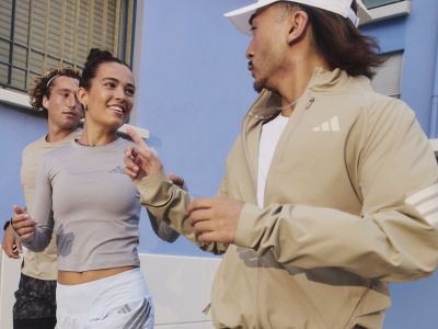 The image shows two people, a man and a woman, engaged in a friendly conversation in what appears to be an urban setting with a blue wall in the background.