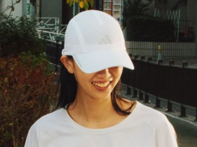 A person wearing a white baseball cap is smiling and standing in front of a building with a metal railing in the background.