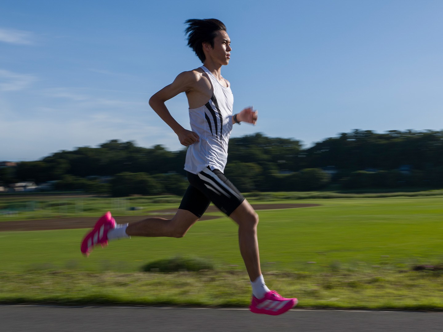 A person in athletic clothing is running on a grassy field with trees and buildings visible in the background.
