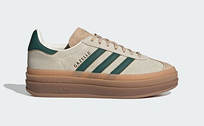 A pair of beige and green Adidas Gazelle platform sneakers with a gum sole against a plain white background.