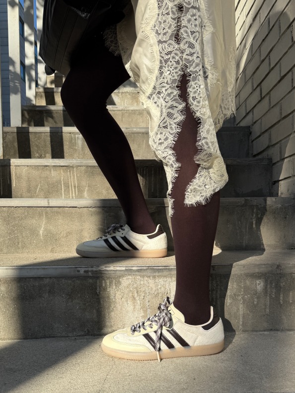 The image shows a person's lower body wearing black leggings and white sneakers, standing on a set of concrete stairs with a lace-trimmed garment draped over the person's legs.