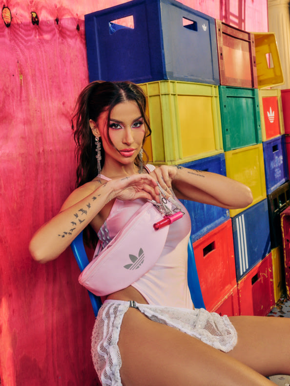 A young woman with dark hair and tattoos poses in front of a colorful, geometric background of stacked crates.