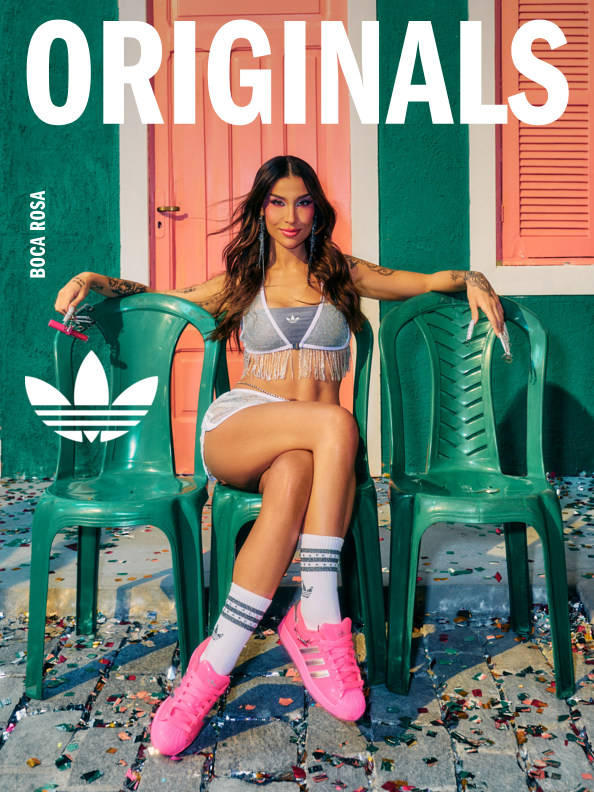 A young woman in a gray sports bra and pink sneakers sits on green plastic chairs against a colorful, textured background.