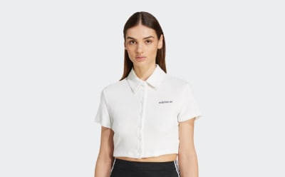 Une jeune femme aux longs cheveux noirs portant une chemise à col blanc se tient sur un fond blanc uni.