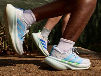 Na zdjęciu widać nogi i stopy osoby w kolorowych sneakerach w sportowym stylu na ziemi lub trawiastej powierzchni.