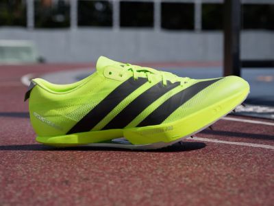 Jaskrawozielono-czarne buty sportowe na czerwonym bieżni, z rozmytym tłem widocznym na budynku.