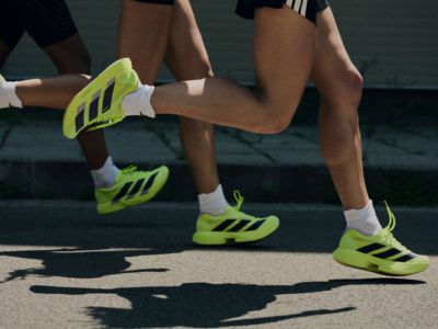 The image shows a person's legs and feet wearing bright green athletic shoes, standing on a surface with shadows cast on it.