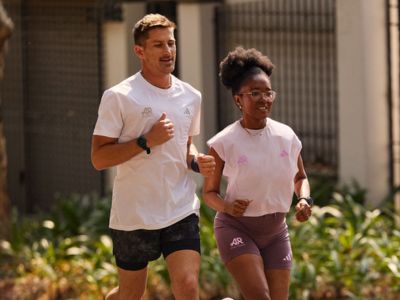 Two people, a man and a woman, are walking together on a path surrounded by greenery.