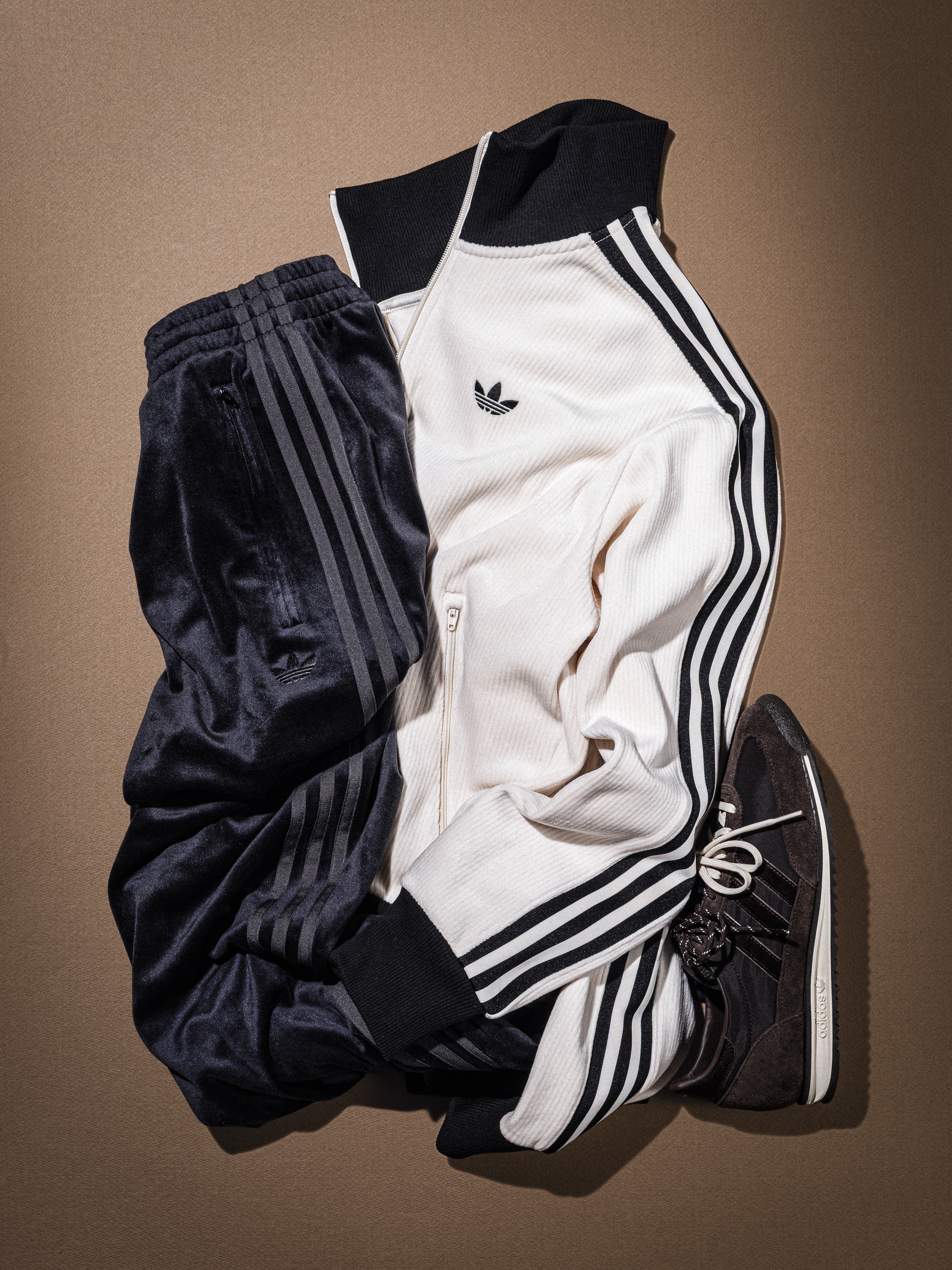 A crumpled black and white Adidas tracksuit lies on a beige background.