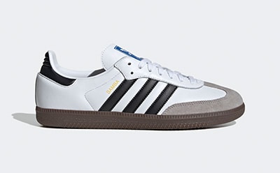 A pair of white, black, and gray Adidas sneakers with a gum sole is the focus of the image, set against a plain white background.
