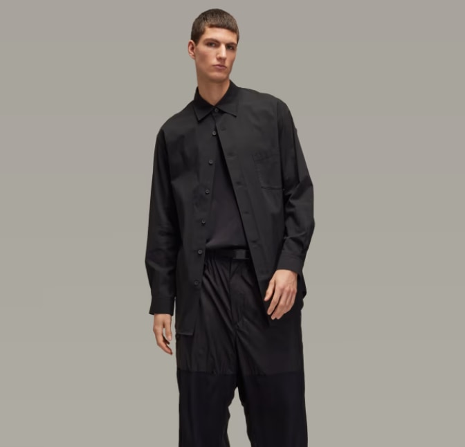 A young man wearing a black jacket and pants stands against a plain gray background.