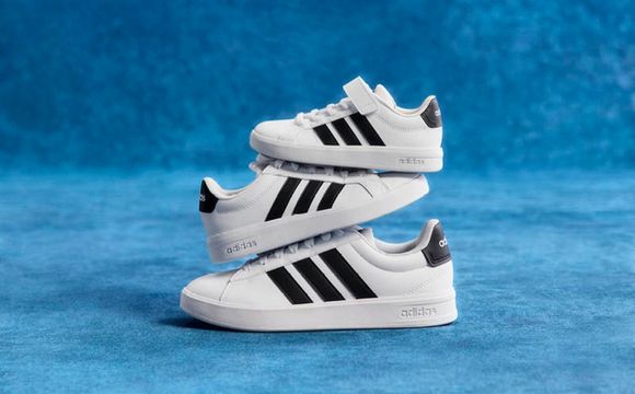 A pair of white and black Adidas sneakers against a vibrant blue background.