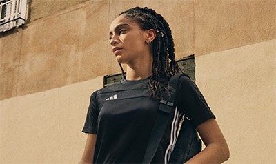 En ung kvinna med flätat hår står framför en beige vägg, iklädd en svart atletisk topp.