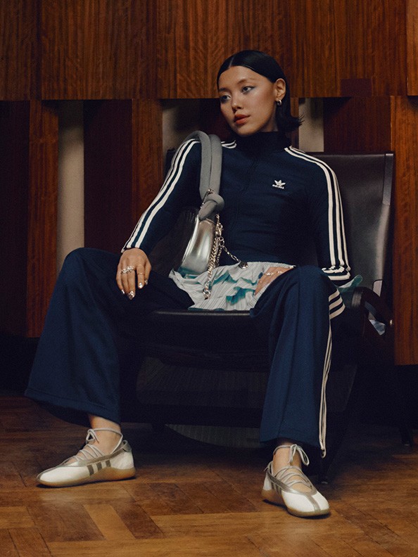 A person wearing a black tracksuit with white stripes sits on a wooden bench in a dimly lit room.