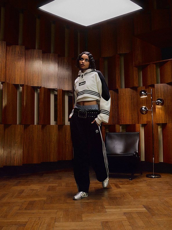 A person wearing a striped sweater and black pants stands in a dimly lit room with wooden paneled walls and a bright light fixture overhead.