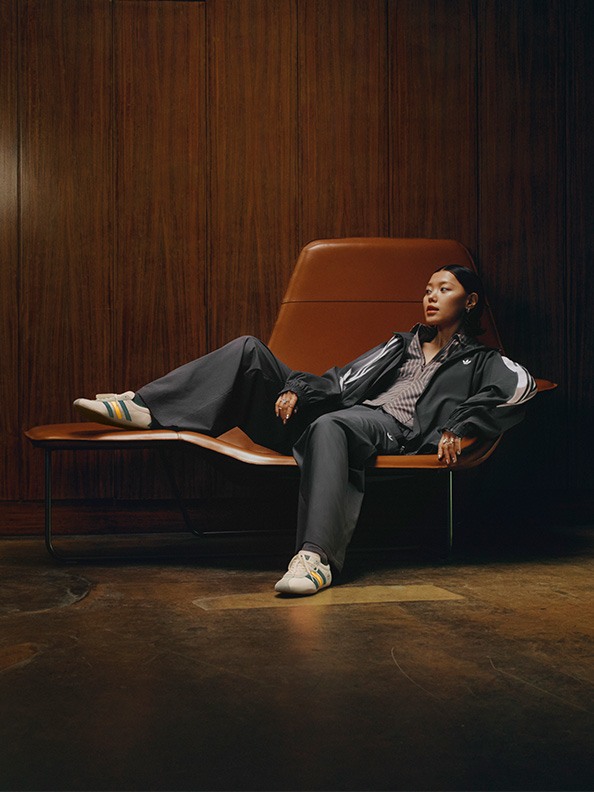 A person in a suit is reclining on an orange couch against a wooden paneled wall.