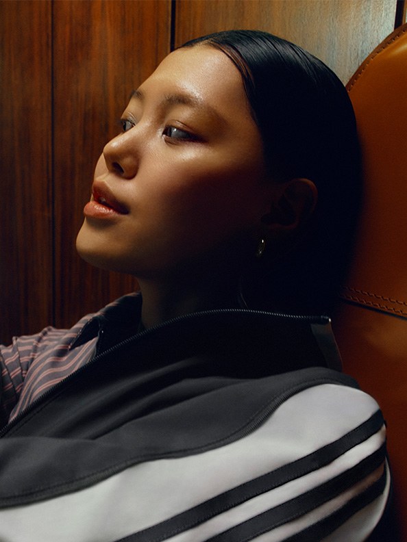 A young woman with dark hair and a pensive expression is captured in a close-up shot, set against a wooden background.