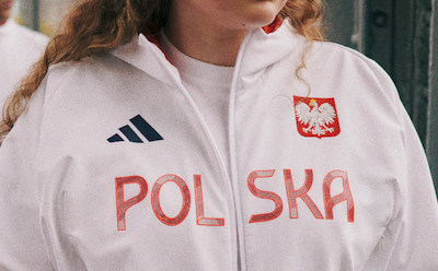 Osoba w białej kurtce z napisem "POLSKA" i polskim godłem narodowym, stojąca na drewnianym tle.