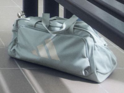 Een grijze sporttas met witte strepen prijkt op een betegelde vloer tegen een donkere achtergrond.