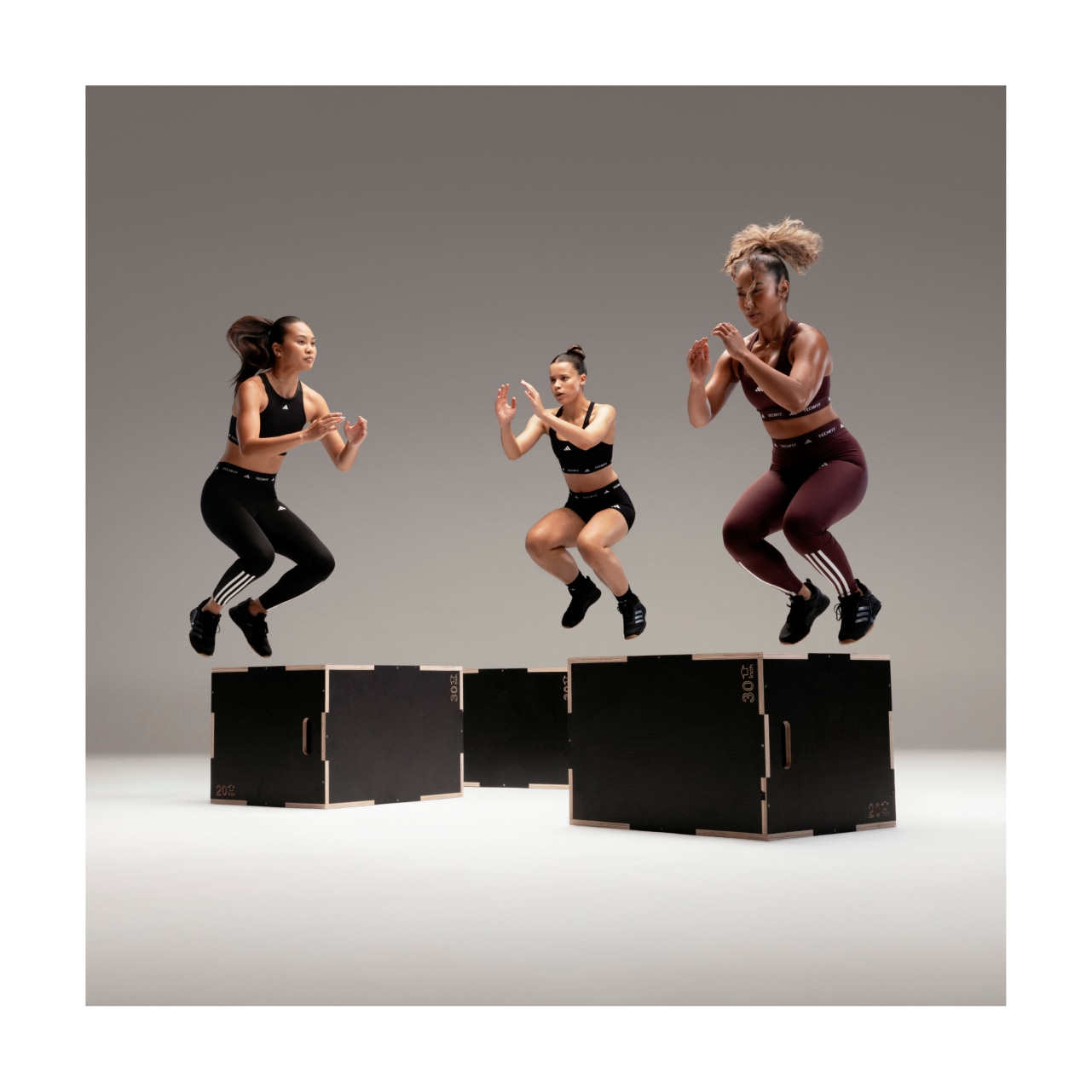 Three women wearing TECHFIT gear perform box jumps.