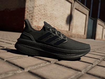 A pair of black Adidas sneakers rests on a brick surface, with a brick wall visible in the background.