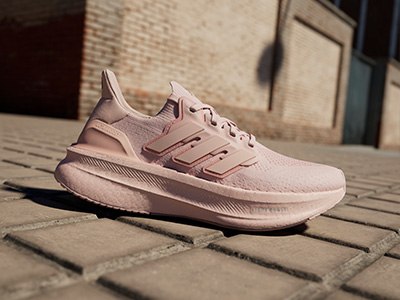 A pair of light pink athletic shoes rests on a brick surface, with a brick wall visible in the background.