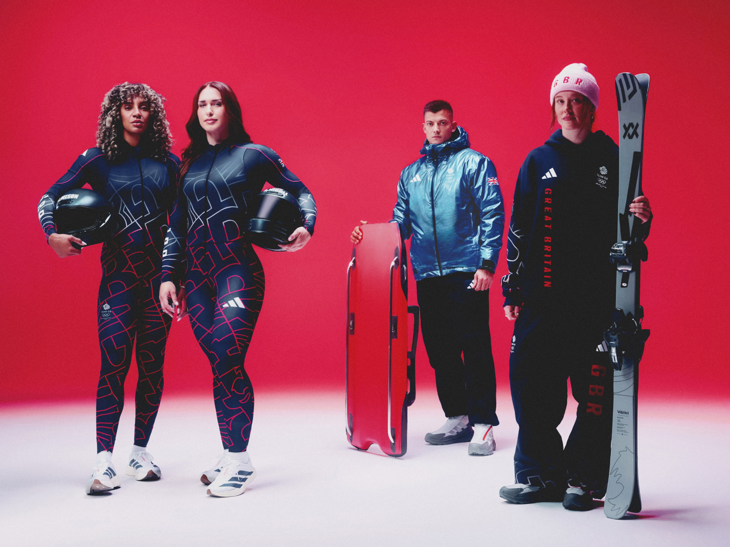 Four individuals, two women and two men, are standing together against a vibrant red background. They are wearing athletic apparel and gear, suggesting they are involved in some kind of winter sports or activities.