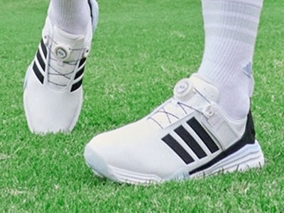 The image shows a pair of white and black athletic shoes on a grassy field.