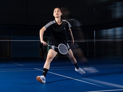 A female athlete in athletic attire stands on a tennis court, holding a tennis racket and preparing to make a shot.