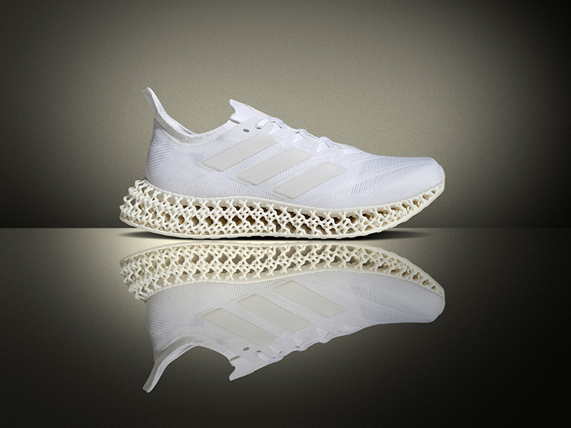 Un par de zapatillas deportivas blancas con un patrón único e elaborado en la suela, que descansa sobre una superficie reflectante sobre un fondo oscuro.