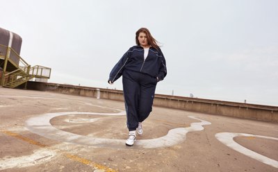A person wearing a navy blue tracksuit walks on a concrete path surrounded by a ramp and other structures in the background.